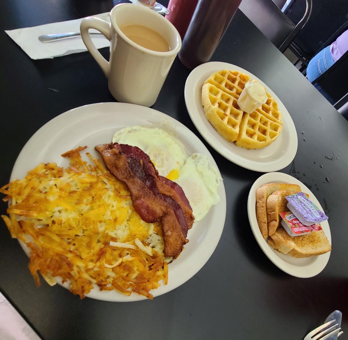 Hash browns, bacon, two eggs, a waffle, toast and a mug of coffee